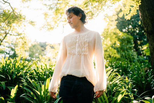 Person in sheer blouse standing among green foliage at golden hour