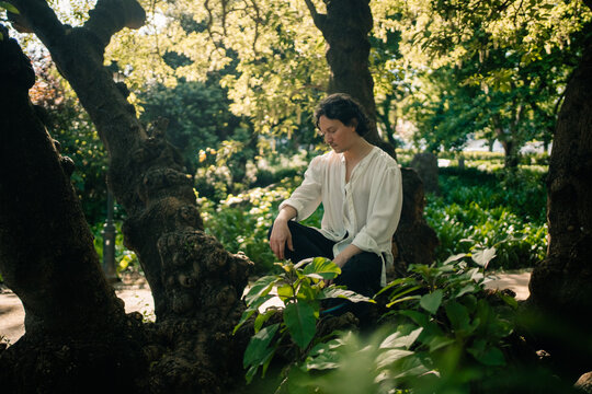 Person sitting thoughtfully on tree in sun-dappled garden