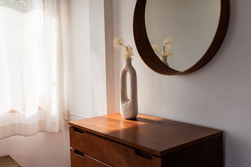 Vase with flowers on dresser beside round mirror in daylight