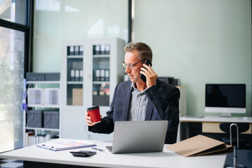 Fototapeta premium businessman in an office with a laptop, tablet, and notes. Ideal for business, finance, accounting