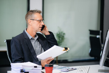 Confident businessman working on finance analysis with a tablet and laptop at office desk. Perfect...