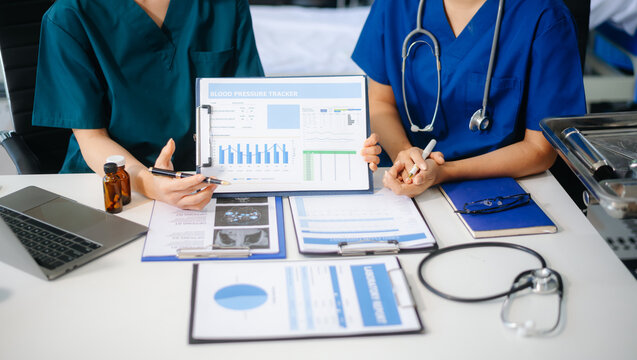 Two doctors and a female nurse meet at a table in the hospital, collaborating on medical tasks using laptops and computers