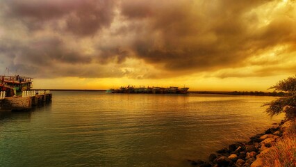 ships anchored at the pier at sunrise with clouds reflecting on the calm sea water