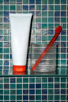 Bathroom shelf with white tube and red toothbrush in a glass. 