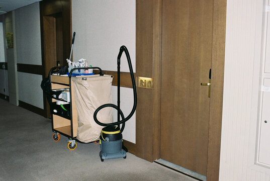 A vacuum cleaner and hotel cleaning cart in the hall.