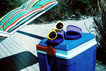 sunlounger, sandals, sunglasses and cooler on the street, 35mm