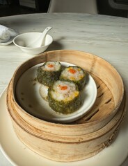 Steamed green seaweed dumplings filled with shrimp and corn, served in a bamboo basket, a modern twist on traditional dim sum