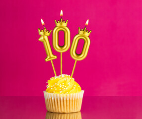 Yellow birthday cupcake with a number 100 candle - Birthday card on a pink background