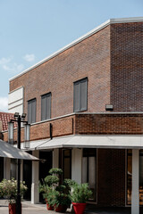 Urban building facade with red brick wall, black shutter windows, white canopy, and green potted...