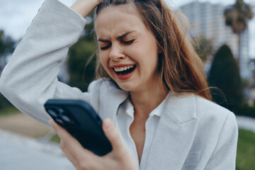 Young woman in light blazer expressing frustration and stress while looking at smartphone screen...