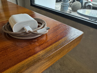 White mobile phone charger with a braided cable coiled on a polished wooden table. Ideal for technology or cafe themes.