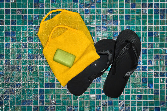 Flip flops and yellow washcloth on blue tiled floor of a shower cabin.