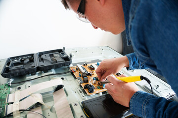 Tv repairman fixing a circuit board using a soldering iron in a disassembled television set
