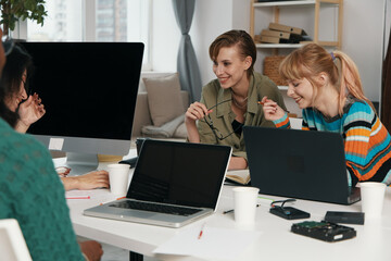 smiling young adult woman and friends socializing at workplace with laptops, business colleagues,...