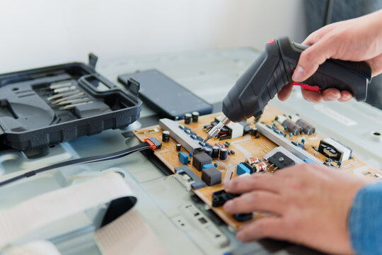 Hands using a power tool to repair a circuit board of a led tv in an electronic workshop