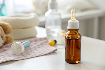 Brown glass dropper bottle with liquid, surrounded by baby care items on a soft surface