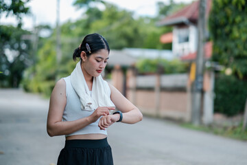 Young woman using a smartwatch while exercising outdoors in a suburban area, focusing on fitness and technology.