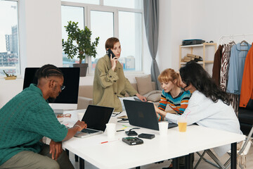 young woman working on phone while colleagues and friends socialize in modern workplace, Gen Z...