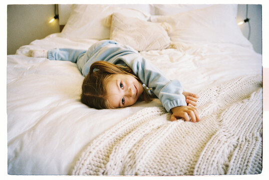 Little Girl Lying on White Bed with Cozy Blanket