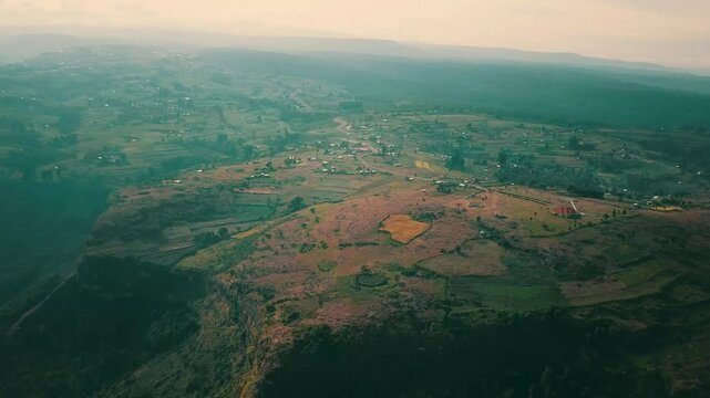 Drone captures cultivated plots and scattered homes along the cliffs of Mount Elgon in Kapchorwa, Uganda, with expansive views of the fertile landscape under soft daylight
