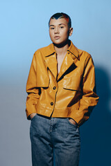 Young woman with short hair wearing a mustard yellow leather jacket and blue jeans stands...
