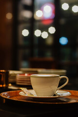 White coffee cup on a small saucer, placed on a wooden tray with blurred lights background