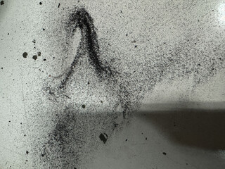 Abstract texture of fine black dust or powder scattered and smeared on a light surface, creating a...