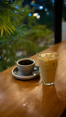 A cup of hot coffee and a glass of ice latte on wooden table with blurred green foliage background