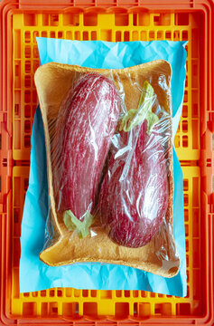 Fresh eggplants wrapped in plastic on bright orange crate