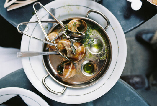 Escargot served with tongs in a dish with herb butter