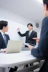 社内打ち合わせでプレゼンをするスーツを着たハンサムな男性ビジネスマン　ホワイトボードの前に立つ話す　縦