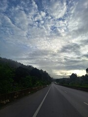 Empty Road at Sunset with Cloudy Sky, Mountain View, and Streetlights in a Calm Rural Area