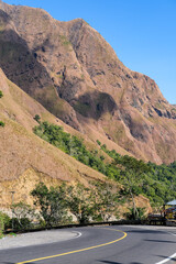 Winding mountain road in Sembalun, Lombok, leading toward Mount Rinjani National Park, surrounded by steep golden hills, dry grassy slopes, and dramatic natural cliffs under a clear blue sky.