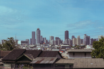 A hazy skyline view of Jakarta reveals layers of high-rise buildings looming behind low residential...