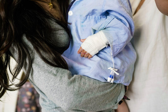 Mother holding sick child in hospital gown with iv catheter