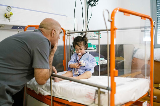 Grandfather comforts granddaughter hospitalized in pediatric clinic - Powered by Adobe