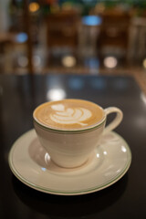 A cup of coffee latte with froth art on the table with blurred background lights