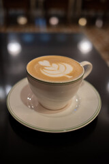 A cup of coffee latte with froth art on the table with blurred background lights