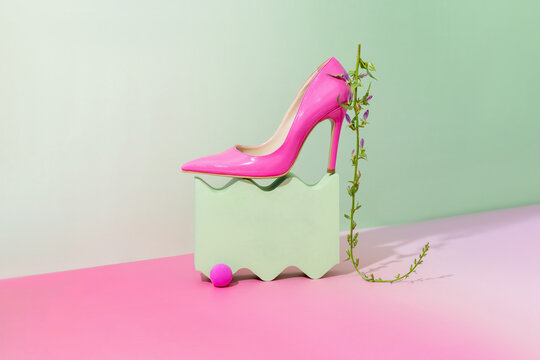 Bright pink high heel shoe on a stylish green pedestal with greenery