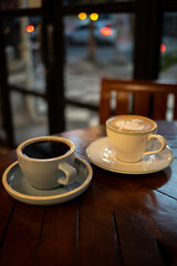 A cup of hot black coffee and hot latte with froth art on the table with blurred traffic background
