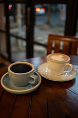 A cup of hot black coffee and hot latte with froth art on the table with blurred traffic background