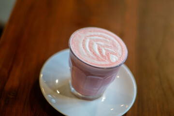 A glass of red velvet latte with froth art on wooden table