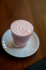 A glass of red velvet latte with froth art on wooden table