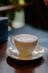 A white ceramic cup filled with a frothy beverage sits on a matching saucer, placed on a dark wooden table