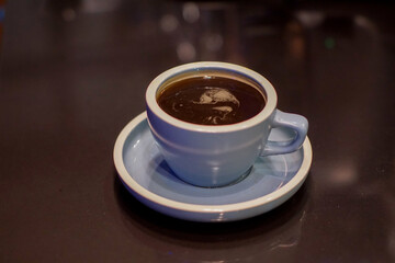 A blue ceramic cup filled with dark coffee rests on a matching saucer