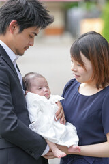 Obraz premium In June 2025, a Japanese couple in their early twenties stands in front of the shrine in Aichi, holding their one-month-old baby together for their omiyamairi, cherishing the moment as a new family.