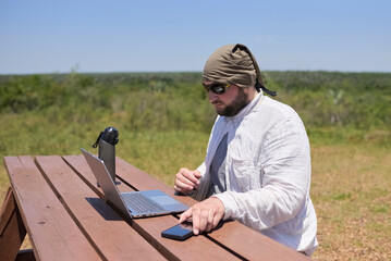 Young Hispanic man working on his laptop at an outdoor table on a sunny day. Concept: digital nomad...