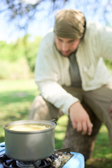 Male traveler waiting for his meal to be ready, rice with vegetables that he is cooking using a gas portable stove, at his campsite. Composition with selective focus on the pot.