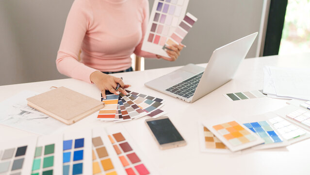 Asian Adult Woman User Interface Designer Choosing Color Palette with Laptop, Smartphone on Desk for Creative Design Process and Inspiration