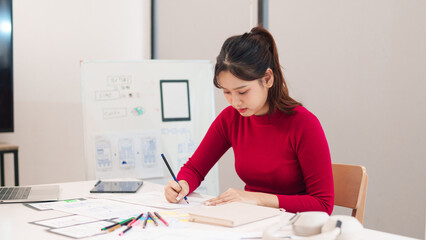 Asian Woman User Interface UI Designer at Desk Sketching Website Wireframes and App Layouts for Mobile Phone with Laptop, Tablet and Whiteboard